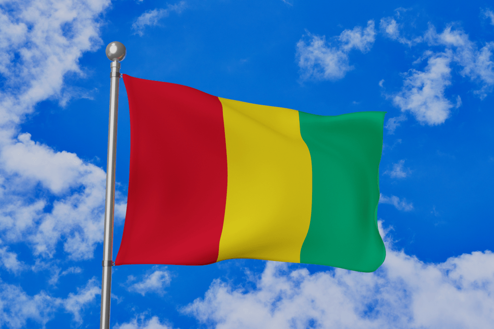 Guinea national flag waving isolated in the blue cloudy sky