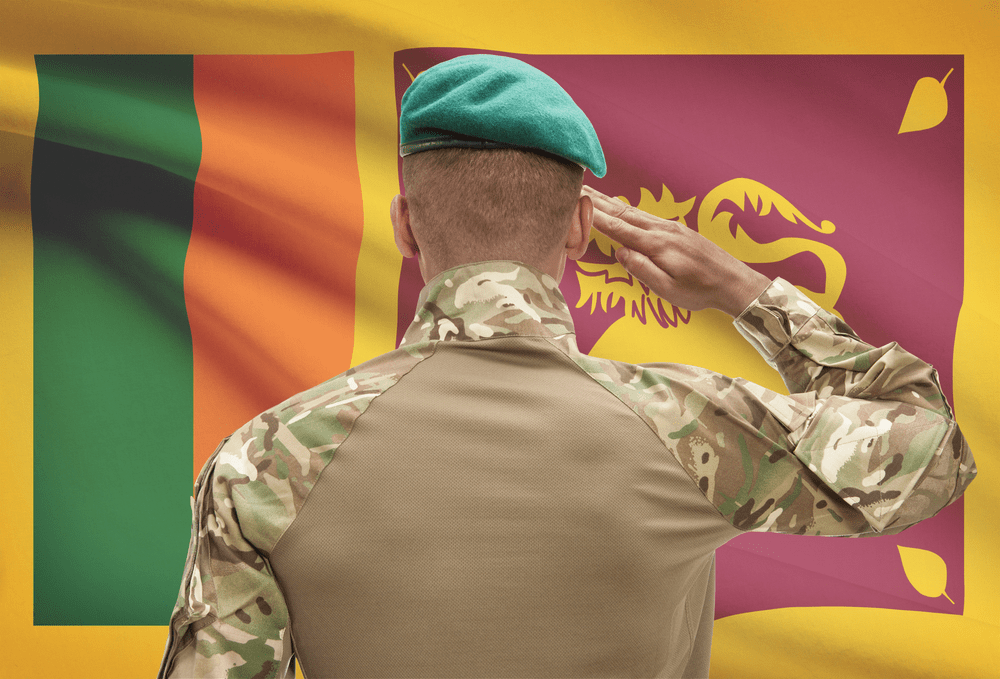 Dark-skinned soldier in hat facing national flag of Sri Lanka